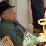 An elderly man and his unusually shaped cane lounge in the sunlight